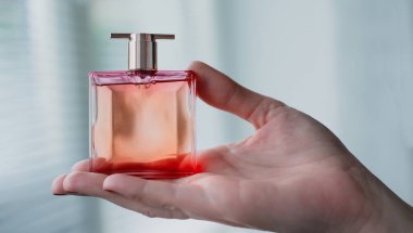 Kadın elinin içindeki parfüm şişesi arka plandaki aydınlatma odasının iç yüzüne karşı. Eau de tuvalet, eau de parfum, güzellik konsepti.