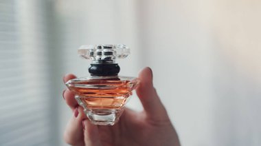 Kadın elinin içindeki parfüm şişesi arka plandaki aydınlatma odasının iç yüzüne karşı. Eau de tuvalet, eau de parfum, güzellik konsepti.