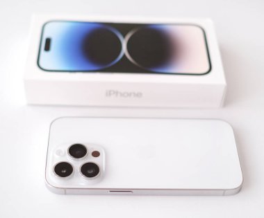 Parnu, Estonia - February 10, 2023: Isolated on white background new IPhone 14 pro in silver color with a triple camera, box, Air Pods and a wire to charge the device. Side view, close-up..