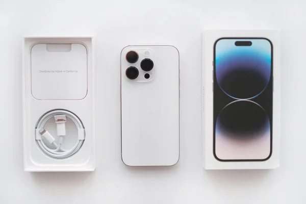 Parnu, Estonia - February 10, 2023: Isolated on white background new IPhone 14 pro in silver color with a triple camera, box and a wire to charge the device. Top view, flat lay..