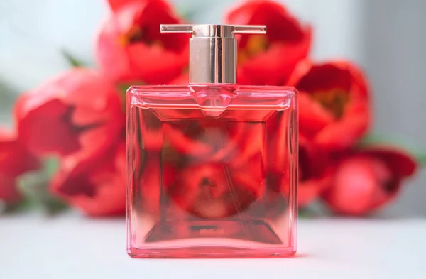 Parfum with flowers on light background. A perfume bottle surrounded by red tulips. Eau de toilette, eau de parfum, beauty concept.