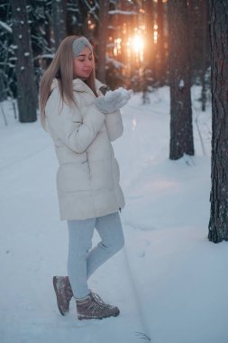 Beyaz ceketli bir kadın kar ormanında gün batımının arka planında.