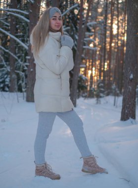 Beyaz ceketli bir kadın kar ormanında gün batımının arka planında.