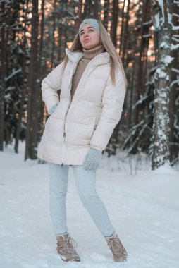 Beyaz ceketli ve şapkalı bir kadın karın üzerinde duruyor..