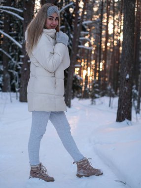 Beyaz ceketli ve şapkalı bir kadın karın üzerinde duruyor..