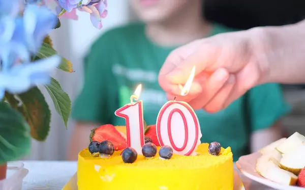 A person lighting a candle on a yellow cake with number 10.