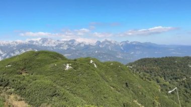 Açık mavi gökyüzü olan bir dağ sırası. Dağlar yeşil ağaçlarla çevrili..