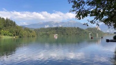 Arkasında dağlar olan güzel bir göl. Su sakin ve berrak. Suda birkaç tekne var ve birkaç kişi manzaranın tadını çıkarıyor.