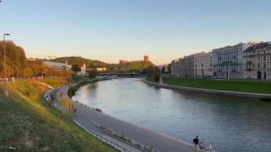 Bir nehir, üzerinde köprü olan bir şehrin içinden akar. Su sakin ve gökyüzü mavi..