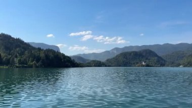 Arkasında dağlar olan güzel bir göl. Gökyüzü açık ve mavi. Su sakin ve durgun..