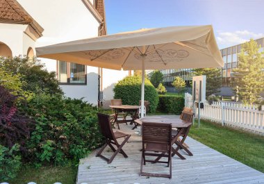 Büyük bir şemsiyesi ve birkaç sandalyesi olan bir teras. Sandalyeler yemek masasının etrafına dizildi..