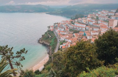 Arka planda bir kasaba olan güzel bir sahil. Su sakin ve gökyüzü bulutlu. Llastres, İspanya.