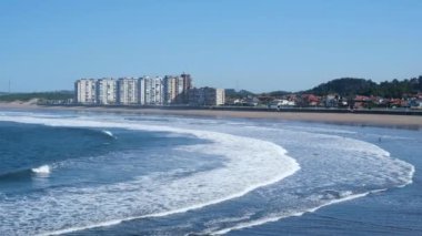 Arkasında büyük bir bina olan bir okyanus plajı. Salinas, İspanya.
