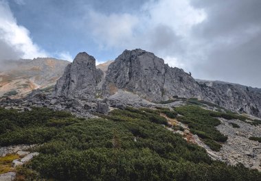 Arkasında bulutlu bir gökyüzü olan bir dağ. Dağ yeşil bitki örtüsüyle kaplı..
