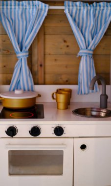 Sobası ve lavabosu olan küçük bir mutfak. Sobanın üzerinde mavi beyaz bir perde asılı.