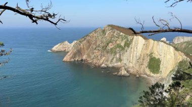 Arka planda bir su kütlesi olan kayalık bir kıyı şeridi. Su sakin ve gökyüzü berrak. Asturias, İspanya