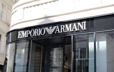 Modern cam mağazası bir Emporio Armani butiği şık bir şehir caddesinde. Lüks moda markaları simgesel kartal logosu ve kalın harfler girişte belirgin bir şekilde sergileniyor..