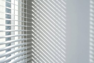 Güneş ışığı, beyaz pencerelerden geçen çizgili gölgeleri temiz bir duvara yansıtıyor. Geometrik ışık desenli minimalist iç mekan, sakin ve modern estetiği çağrıştırıyor..