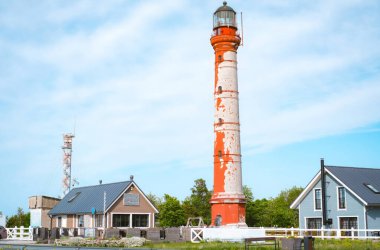 Estonya 'daki kırsal kırmızı-beyaz Pakistan deniz feneri küçük samimi binalar ve yemyeşil alanlarla çevrili parlak mavi bir gökyüzüne karşı dimdik ayakta duruyor. Bu kıyı sahnesi cazibeyi, tarihi ve denizciliği çağrıştırıyor.