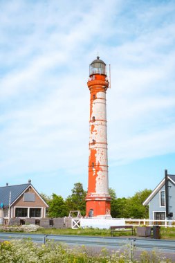 Estonya 'daki kırsal kırmızı-beyaz Pakistan deniz feneri küçük samimi binalar ve yemyeşil alanlarla çevrili parlak mavi bir gökyüzüne karşı dimdik ayakta duruyor. Bu kıyı sahnesi cazibeyi, tarihi ve denizciliği çağrıştırıyor.