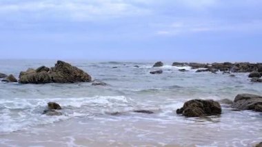 İspanya 'nın Asturias kentindeki dinamik deniz manzaralı kayalara çarpan okyanus dalgalarının yakın görüntüsü. Görüntü, deniz köpüğünün enerjisini yakalar ve yumuşak bulutlu gökyüzü altında su sıçratır.