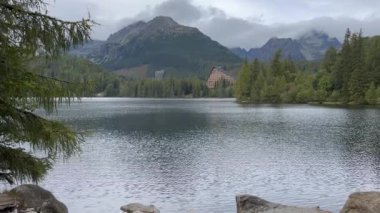 Slovakya 'nın High Tatras dağlarındaki Strbske Pleso gölünün manzarası. Sakin suları, bir çam ormanı ve bulutlu bir gökyüzünün altında görkemli zirveleri olan sakin bir dağ manzarası. Meşhur otel görünüyor.
