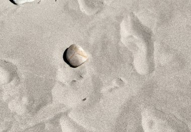 Pürüzsüz, açık renkli tek bir taş ince, açık renkli geniş bir kumun üzerinde uzanır ve minimalist ve sakin doğal bir zemin oluşturur. Yumuşak gölgelerin ve dokuların etkileşimi