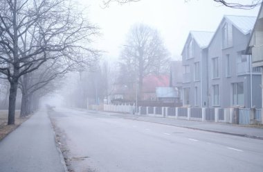 Çıplak ağaçlar ve gri İskandinav tarzı binalarla bomboş sisli bir cadde, sessiz ve melankolik bir atmosfer yaratıyor. Parnu, Estonya. Sis, şehir manzarasına gizemli ve yalnız bir hava katıyor..