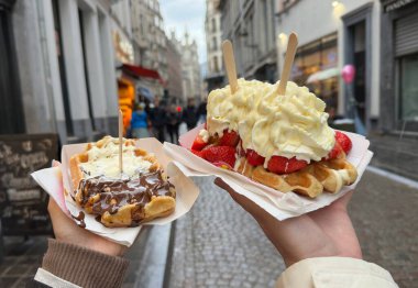 Brüksel 'in büyüleyici sokaklarını keşfederken üzerinde krema, taze çilek ve çikolata sosu olan iki lezzetli Belçika waffle' ının tadını çıkarıyorum. Şehir yürüyüşü için harika bir ikramdı..