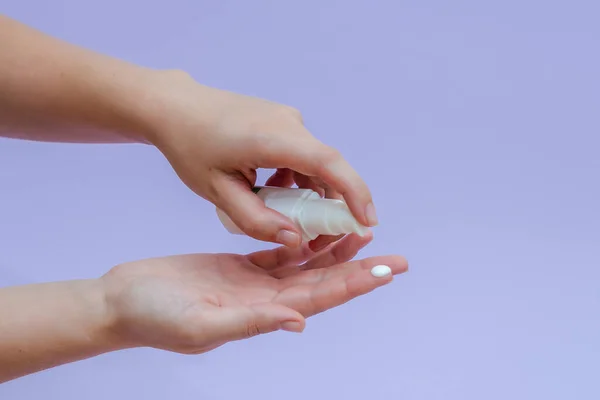 Woman's hand squeezing out cream in white tube isolated on lilac background. Beauty concept. Tube for cosmetic products
