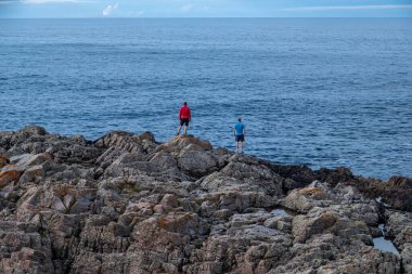 Atlantik Okyanusu 'na bakan arkadaşlar, alçak gelgit (ebb), Portskerra limanı, Kuzey İskoçya, Melvich yakınlarındaki bir kayanın kenarında duruyorlar.