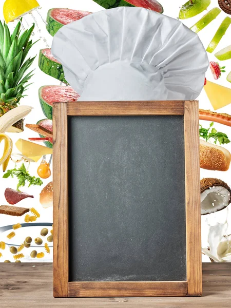 Chef Hat over Empty Blackboard with Food Ingredients Background