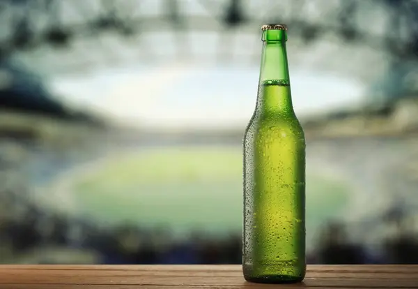 Botol Beer Hijau Dingin Permukaan Wooden Dengan Stadion Latar Belakang Stok Foto