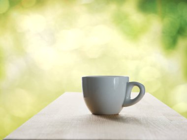 Beyaz seramik kahve fincanı yeşil bokeh arka planlı ahşap masanın üzerinde.
