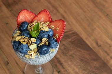 Çilekli Chia tohumu pudingi, yaban mersini, granola ve nane şekeri ahşap bir masada bir bardakta.