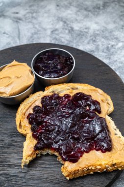 Fıstık ezmesi ve böğürtlen reçelli tost ve kesme tahtasında bir ısırık. dikey biçim.