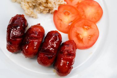Kahverengi pirinç ve domates dilimleriyle servis edilen dört tatlı longaniza..