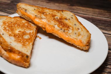 Izgara peynirli sandviç arka planda ahşap masa ile beyaz bir tabakta servis edilir..