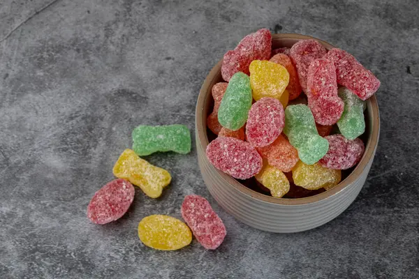Renkli ekşi şekerlerle dolu bir kase dokulu arkaplanda.