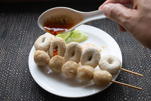 Someone\'s hand is pouring sweet and spicy sauce onto meatballs that local street food of Thailand.