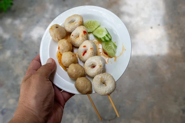 Top view of someone\'s hand holding a white plate of pork balls and fish balls each.