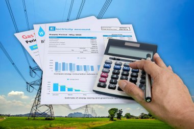 Birisi hesap makinesine basıyor ve elektrik faturaları arka planda yüksek gerilimli elektrik direkleriyle birbirine çarpıyor..