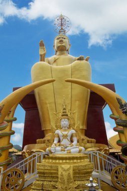 Büyük bir Buda heykeli oturur ve kutsanır. Önde başka bir Buda heykeli oturur..