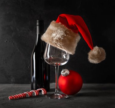 Bir şişe şarap, köknar dallarının arka planında Noel Baba şapkası olan bir bardak. Noel kompozisyonu.