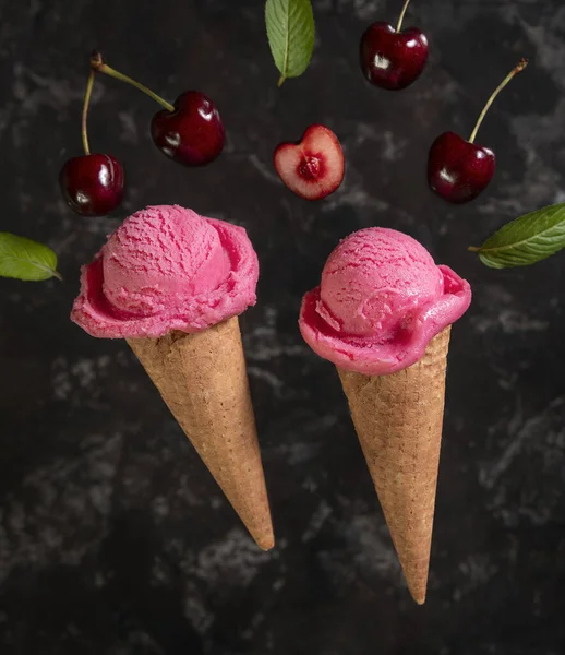 Two cherry ice creams in a waffle cone with cherries