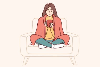 Omuzlarında battaniyesi olan bir kadın neşelenmek ve sıcak ve rahat bir atmosferde rahat hissetmek için sıcak çay içer. Kız tatlı tatlı gülüyor ve üniversiteye gitmeden önce güç kazanmak için sıcak kahve içiyor.