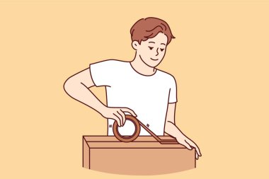 Man packs personal belongings into cardboard relocation box and seals lid with tape. Positive guy small business owner holding box and preparing goods ordered by customer for shipment clipart