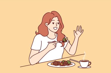 Kadın kafede yemek yiyor masada oturuyor ve garsonu aramak için elini kaldırıyor. Cafe ziyaretçisi kız yağ ve kalorik gıdaların geçmesini önlemek için buğulanmış sebze yiyor.