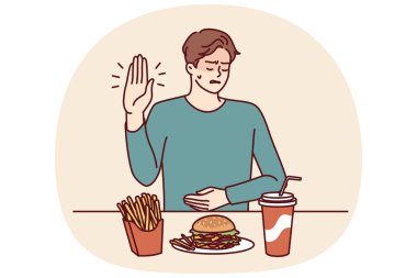 Gastrit hastası bir adam beslenme uzmanının tavsiyesi üzerine karın ağrısına neden olan fast food 'u reddediyor. Masanın yanındaki abur cubur yiyen adam, hamburger yemekten kaynaklanan mide iltihabından dolayı jesti durdurduğunu gösteriyor.