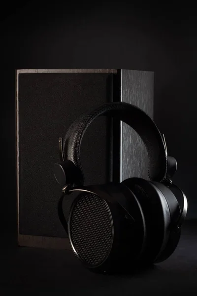 Black headphones and a black speaker on a black background. Music concept